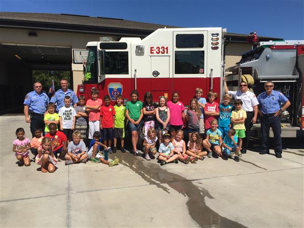 happy students with firemen stand in front of large firetruck